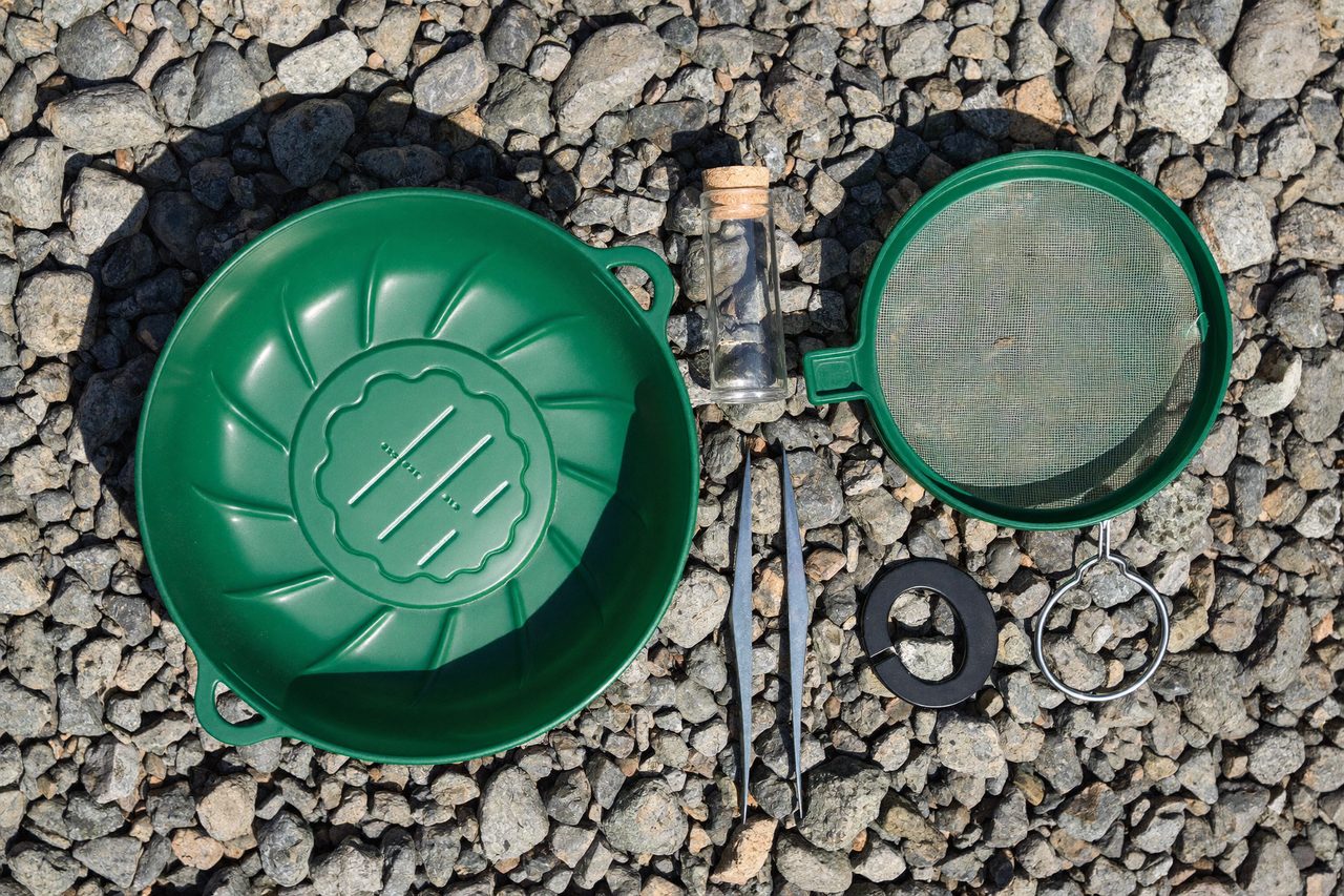 Gold pan, classifier sieve, vial, tweezers and magnet on river gravel
