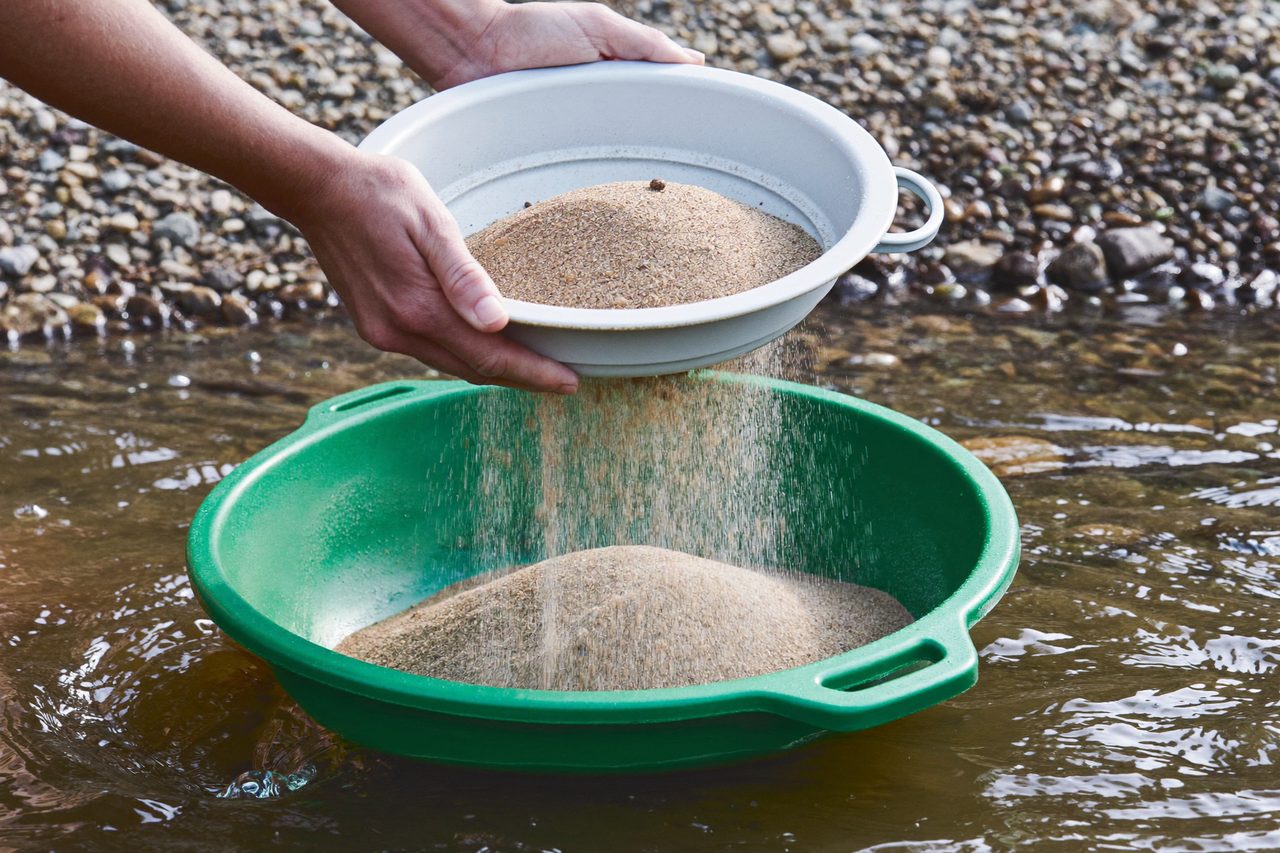 Hands holding a sieve over the gold pan at the river